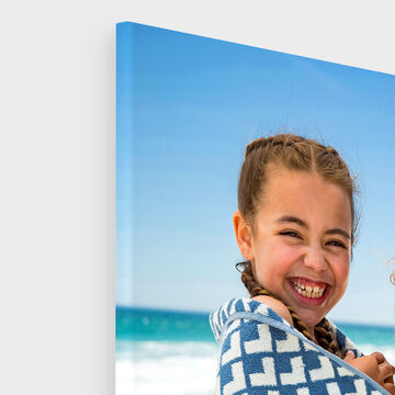 Iemand houdt een CEWE fotoboek vast op een strand met een mooie blauwe lucht.