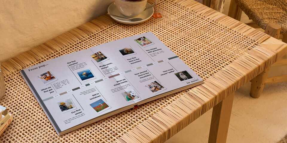 Open CEWE fotoboek op rotanachtige tafel, foto's en teksten zichtbaar.