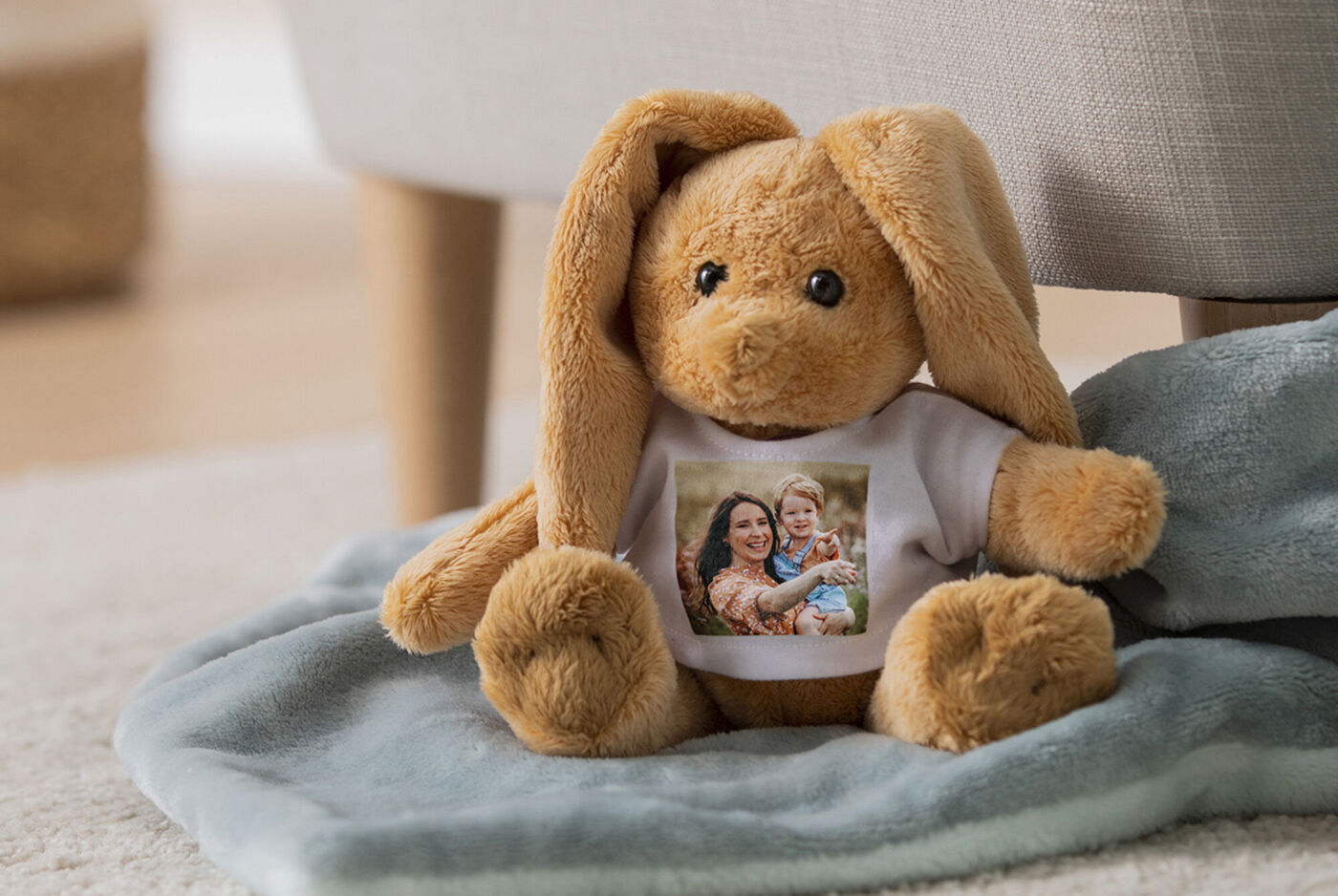 Een schattige knuffelkonijn met T-shirt met een foto van twee personen, liggend op een zachte deken.