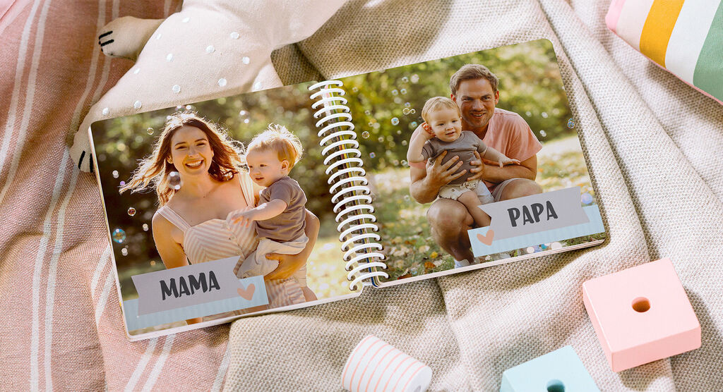 Het beeld toont een geopend fotoboek met een liefdevolle familie foto scène. Links een moeder met kind, rechts een vader met kind. Groene en zonnige achtergrond