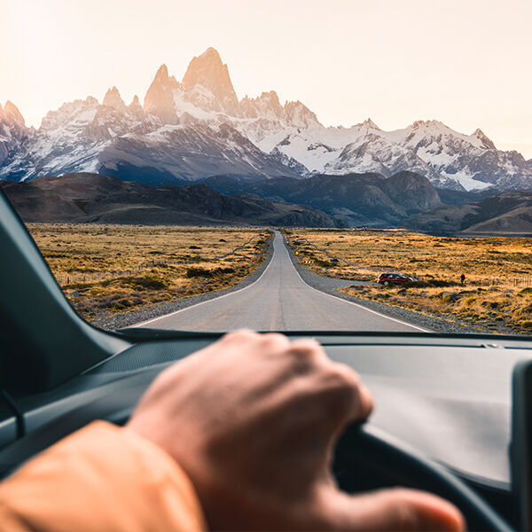 Uitzicht vanuit een auto op een bergweg met majestueuze toppen op de achtergrond.