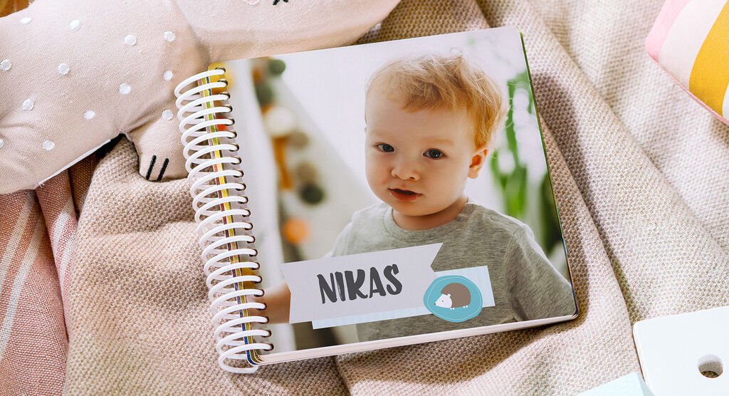 Een CEWE fotoboek op een deken, omringd door speelgoed. De naam 'Niklas' staat op de kaft.