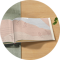 Een geopend CEWE FOTOBUCH met zachte, lichte pagina's en delicate bloemenpatronen. Het ligt op een lichte houten tafel.