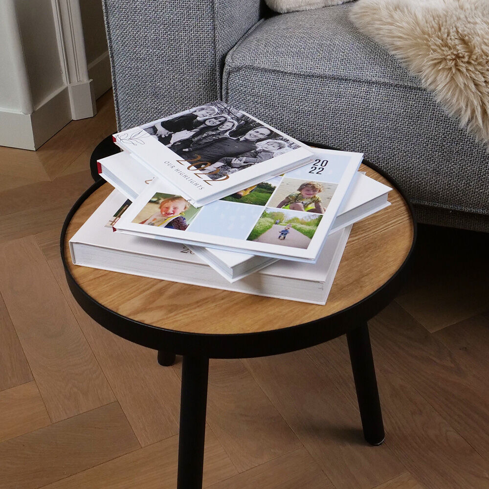 Een stijlvolle woonkamer toont een ronde tafel met verschillende CEWE FOTOVOEKEN. Er ligt een geopend boek op de tafel.