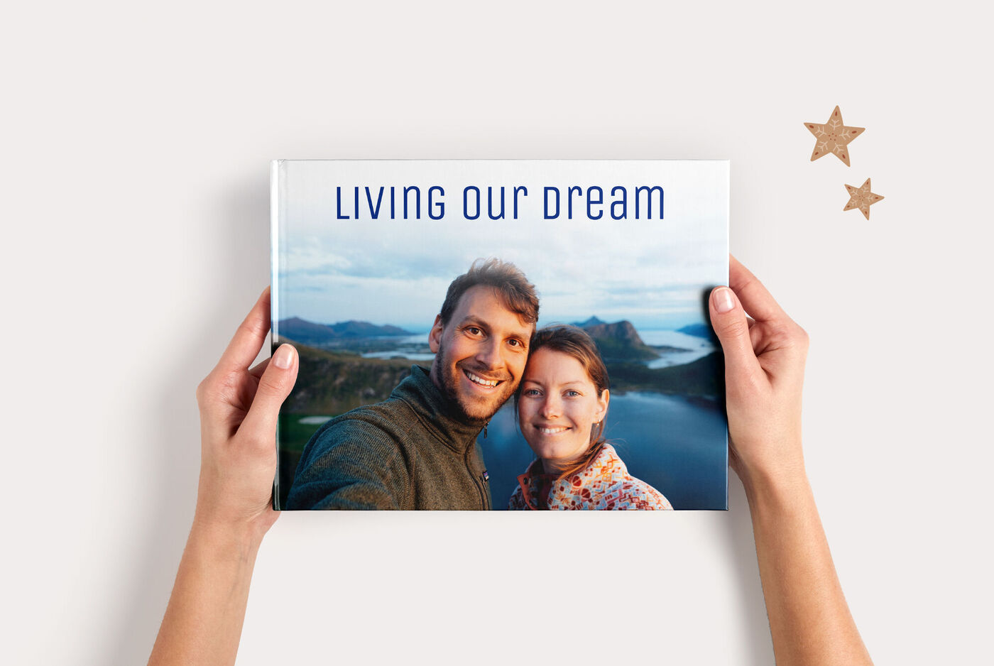 Iemand houdt een CEWE FOTOBOEK vast met een blauwe cover en de tekst 'Living our dream'.'.